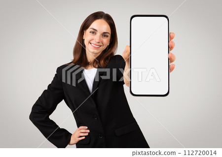Cheerful professional woman presenting a blank smartphone screen, perfect for mockups or ad 112720014