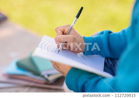 Closeup of notebook in student guy's hands taking notes outdoors 112720015