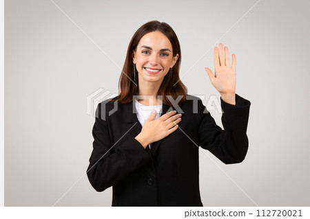 Pleasant businesswoman with a sincere smile raises her right hand to take an oath or pledge Pleasant businesswoman with a sincere smile raises her right hand to take an oath or pledge 112720021