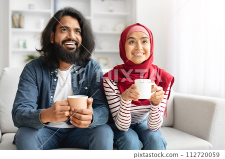 Happy Muslim Couple Drinking Coffee And Relaxing On Couch In Living Room 112720059