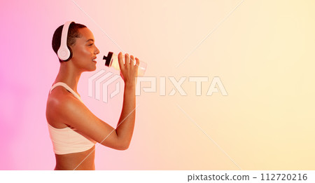 Profile of a smiling athletic woman wearing headphones and drinking water from a bottle Profile of a smiling athletic woman wearing headphones and drinking water from a bottle 112720216