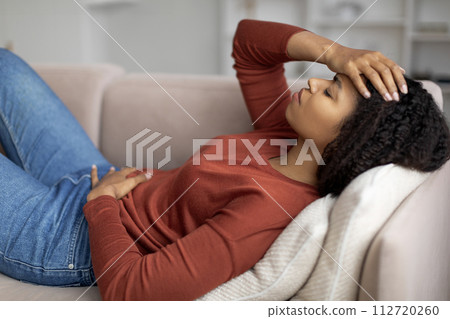 Sick black woman lying on couch, feeling unwell at home Sick black woman lying on couch, feeling unwell at home 112720260