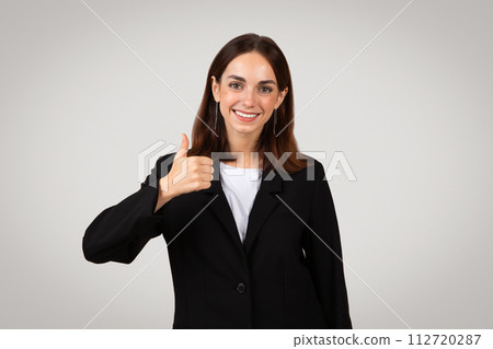 Smiling businesswoman in formal attire giving a thumbs-up as a sign of success 112720287