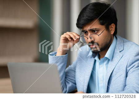 Indian man dealing with eyesight issues squints at laptop indoor 112720328