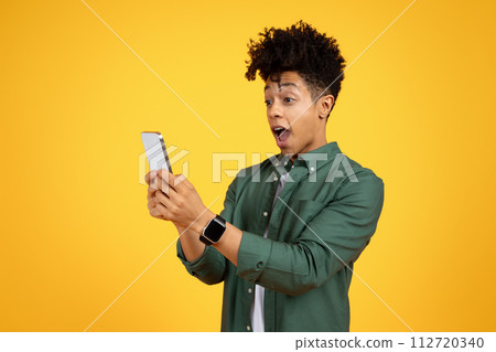 Shocked young black guy looking at cell phone screen Shocked young black guy looking at cell phone screen 112720340