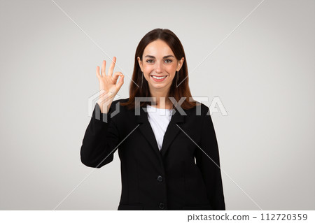 Cheerful young businesswoman in a smart black suit making a positive 'okay' hand sign 112720359