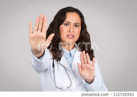 Young lady doctor making stop gesture, keeping hands to defend, protect herself, standing on gray background 112720393
