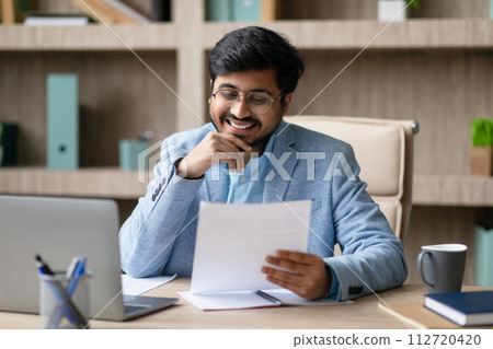 Indian Businessman Engaging In Paperwork Holding And Reading Document Indoor Indian Businessman Engaging In Paperwork Holding And Reading Document Indoor 112720420