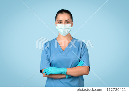 Young woman nurse in scrubs with mask and gloves on blue backdrop Young woman nurse in scrubs with mask and gloves on blue backdrop 112720421