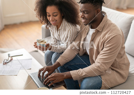 Black couple engaged with paperwork and laptop in living room 112720427