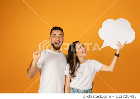 Enthusiastic young man and woman in white shirts holding a blank speech bubble sign 112720485