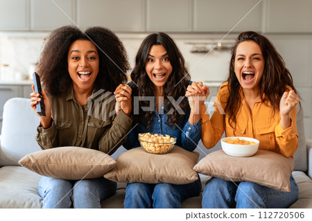 Three emotional diverse women cheerfully shouting reacting watching TV indoor 112720506