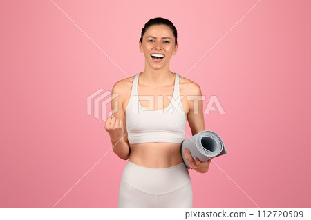 Exuberant young woman in white yoga attire holding a rolled-up yoga mat, ready for a workout session Exuberant young woman in white yoga attire holding a rolled-up yoga mat, ready for a workout session 112720509