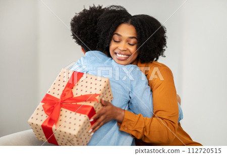 Radiant African American woman with a bright smile hugs a man while holding a gift 112720515