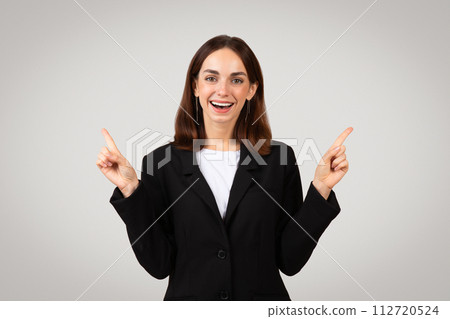 Cheerful businesswoman with a beaming smile pointing both fingers upwards to highlight a new idea Cheerful businesswoman with a beaming smile pointing both fingers upwards to highlight a new idea 112720524