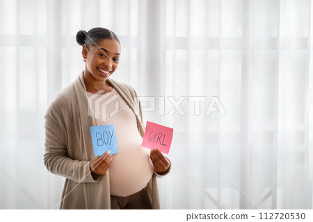 Positive african american pregnant woman showing boy and girl cards 112720530