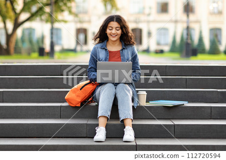 Smiling indian student woman sitting on stairs working on laptop 112720594