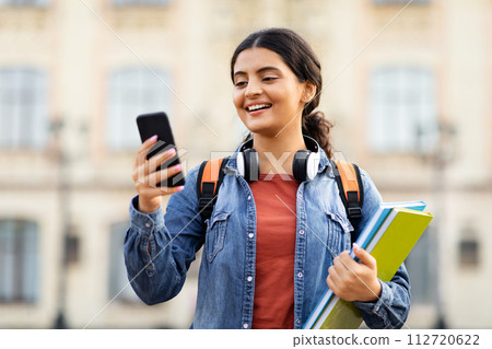 Happy young indian lady student using phone outdoors Happy young indian lady student using phone outdoors 112720622