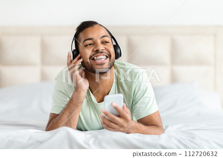 Positive african american guy listening to music in bedroom Positive african american guy listening to music in bedroom 112720632