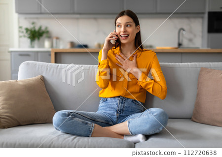 Excited young woman on phone call, sitting on sofa 112720638