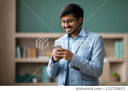 Successful Hindu businessman uses his cellphone in modern office setting Successful Hindu businessman uses his cellphone in modern office setting 112720653