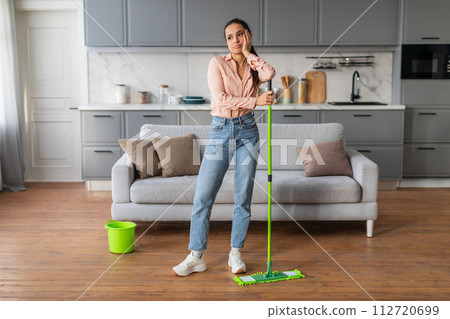 Bored woman leaning on mop in clean kitchen 112720699
