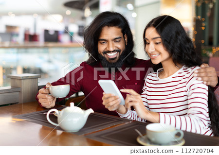 Cheerful loving indian couple have date at cafe, using phone 112720704