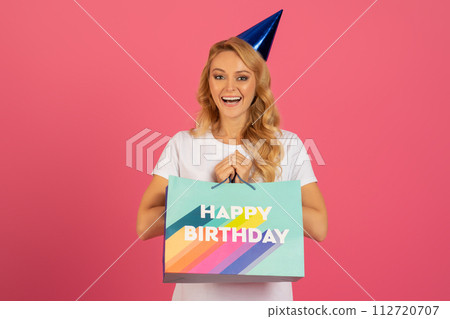 lady joyfully holds her birthday gift against pink studio backdrop lady joyfully holds her birthday gift against pink studio backdrop 112720707