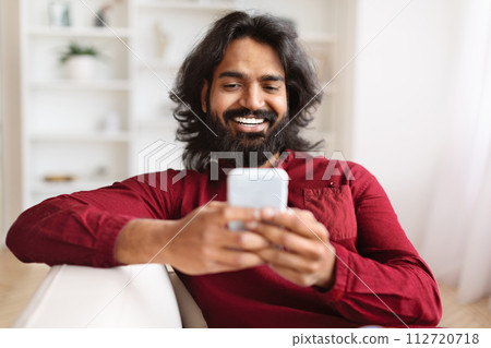 Closeup of cheerful indian guy using smartphone at home 112720718