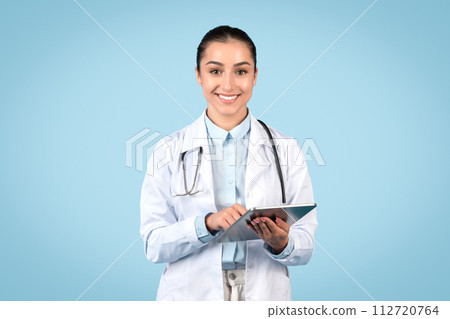 Confident woman doctor using tablet on blue 112720764