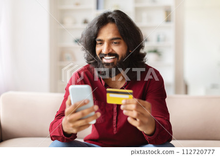 Happy indian man using smartphone and credit card at home Happy indian man using smartphone and credit card at home 112720777