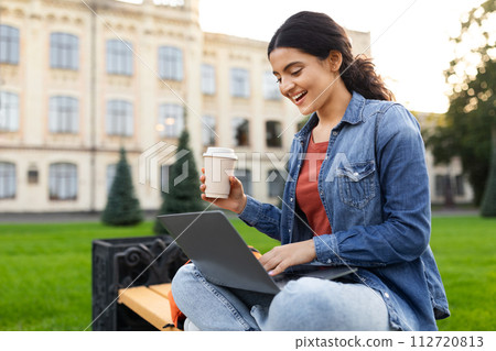 Pretty young indian woman sitting on bench, studying, using laptop Pretty young indian woman sitting on bench, studying, using laptop 112720813