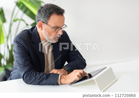Serious and focused mature businessman with glasses intently using a tablet 112720868