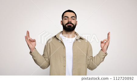 A man with a beard and closed eyes raises both index fingers upwards 112720892