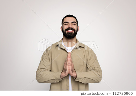 A cheerful man with a neat beard and a bright smile makes a prayer gesture A cheerful man with a neat beard and a bright smile makes a prayer gesture 112720900