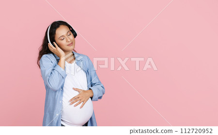 Relaxed pregnant woman listening to calm music and smiling Relaxed pregnant woman listening to calm music and smiling 112720952