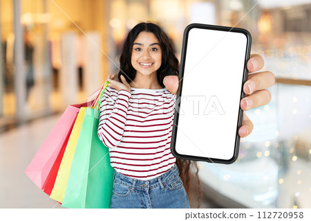 Cheerful eastern woman shopaholic showing phone with blank screen 112720958