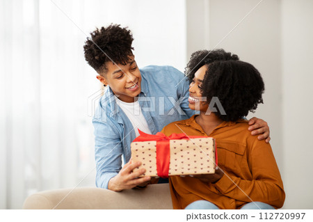 A delighted woman with a wide smile receives a polka-dotted gift box with a red bow from a man A delighted woman with a wide smile receives a polka-dotted gift box with a red bow from a man 112720997
