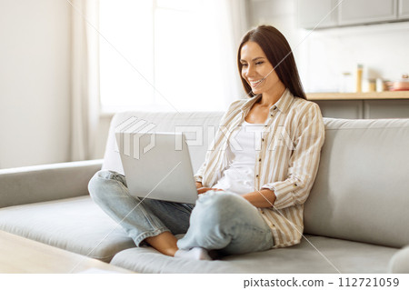 Relaxed woman enjoying working from home, comfortably using her laptop at home Relaxed woman enjoying working from home, comfortably using her laptop at home 112721059