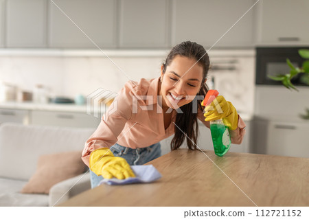 Smiling young woman cleaning kitchen table with spray 112721152