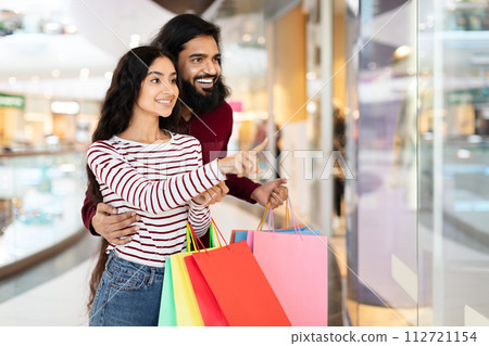 Loving young eastern couple standing in shopping mall with purchases 112721154