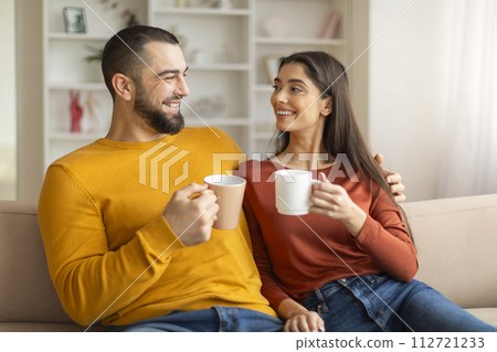Young couple drinking coffee together, sitting on couch in living room Young couple drinking coffee together, sitting on couch in living room 112721233