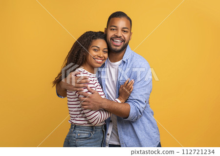 Loving black couple in warm embrace posing against yellow background Loving black couple in warm embrace posing against yellow background 112721234