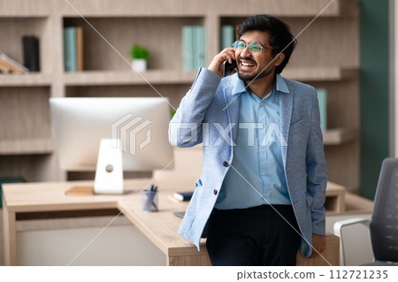 Smiling middle eastern businessman discussing details over phone at office Smiling middle eastern businessman discussing details over phone at office 112721235