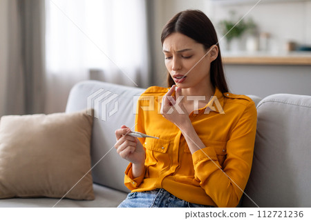 Worried woman checking temperature with thermometer Worried woman checking temperature with thermometer 112721236