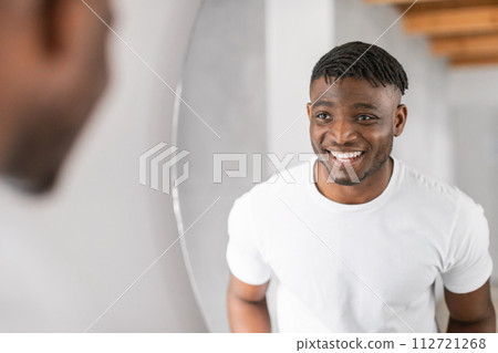 Black man smiling to his reflection in mirror in bathroom Black man smiling to his reflection in mirror in bathroom 112721268