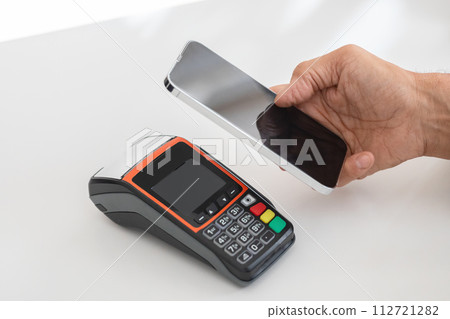 A hand holding a smartphone over a payment terminal, ready to process a contactless mobile payment A hand holding a smartphone over a payment terminal, ready to process a contactless mobile payment 112721282