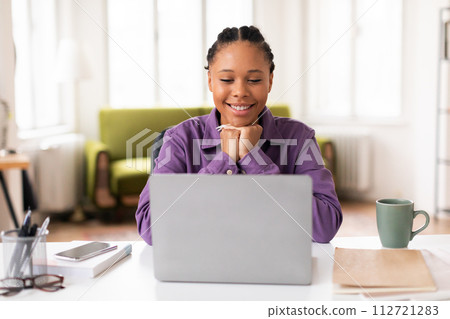 Cheerful black lady student with laptop in purple shirt, studying at home Cheerful black lady student with laptop in purple shirt, studying at home 112721283