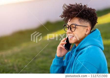 Side view of cheerful brazilian guy chatting on smartphone outside 112721300