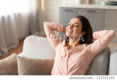 Relaxed woman with her hands behind her head sitting couch Relaxed woman with her hands behind her head sitting couch 112721319